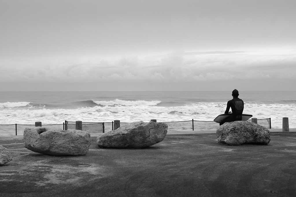 Seul assis sur un rocher un surfeur observe les vagues.